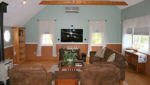 A cozy living room with a wooden ceiling, a flat-screen TV, a fireplace with a 'RELAX' sign, and a brown leather sofa. - PRIVATE HOME NEAR BEACH LOCATED IN NARRAGANSETT, RI (Narragansett)