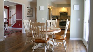 A dining area with a wooden table and chairs, a kitchen in the background, and a staircase leading to another room. - PRIVATE HOME NEAR BEACH LOCATED IN NARRAGANSETT, RI (Narragansett)