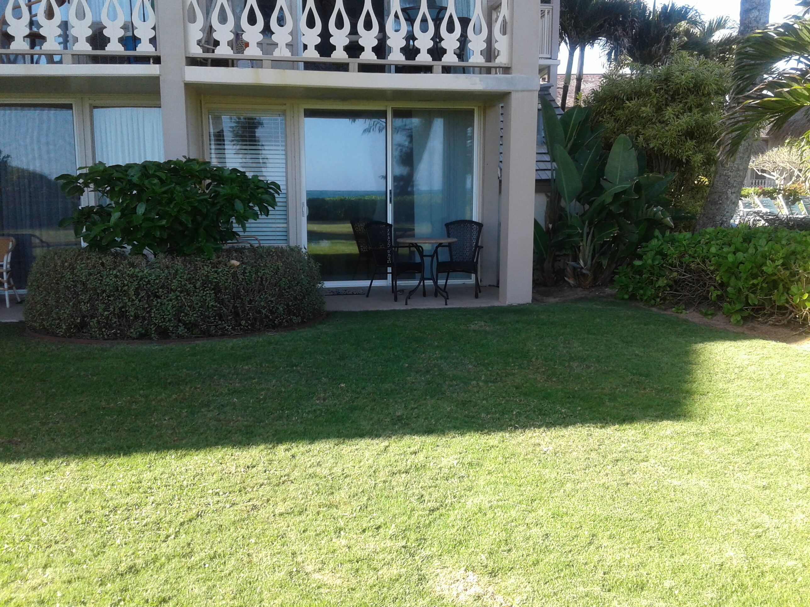A building with a covered patio area, a small lawn, and a seating arrangement.