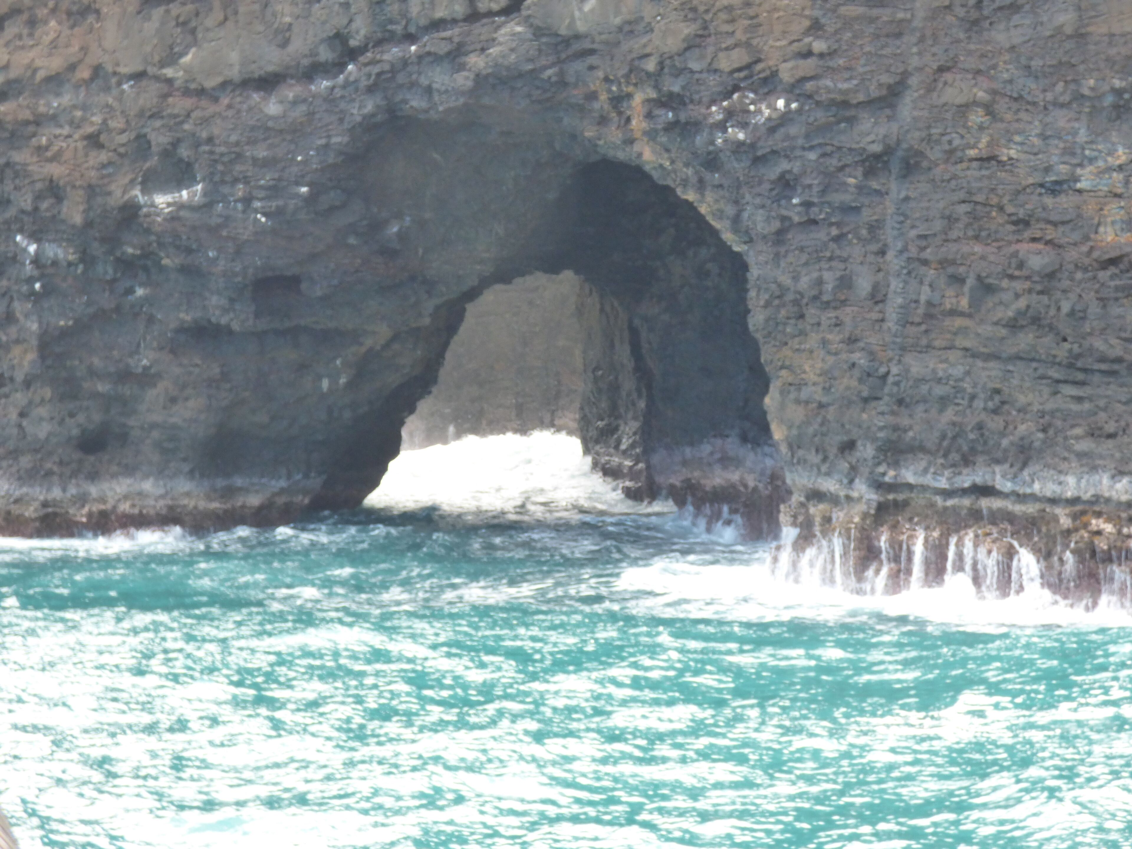 A natural rock formation with a large arch over turquoise water.