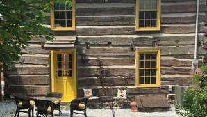 A log cabin with a yellow door and windows, a gravel driveway, and outdoor furniture. - Thaddeus Stevens' Gettysburg Log Home (Gettysburg)