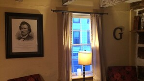 A cozy room with two floral-patterned armchairs, a framed portrait on the wall, and a window with curtains. - Thaddeus Stevens' Gettysburg Log Home (Gettysburg)