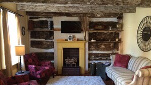 A rustic living room with exposed wooden beams, a fireplace, and a mix of patterned and striped furniture. - Thaddeus Stevens' Gettysburg Log Home (Gettysburg)