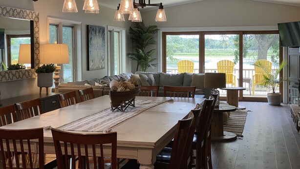A dining area with a large table, chairs, and a chandelier. There is a sofa and a plant in the background. - The Perfect Green Lake Family Getaway (Green Lake)
