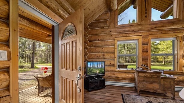 A log cabin interior with a wooden door, a television, a desk, and large windows. - Steps to the River! River Edge Cabin (West Glacier)