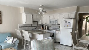 Une cuisine compacte avec des meubles blancs, un four à micro-ondes, un four et un réfrigérateur. Il y a également un coin repas avec une table et des chaises.