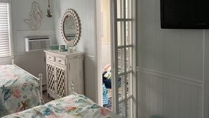Une chambre avec deux lits, une commode, un miroir, un téléviseur et une fenêtre avec des stores.