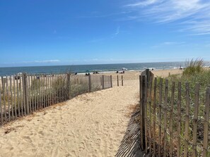 Un sentier de plage sablonneux, bordé d’une clôture en bois, avec vue sur l’océan.