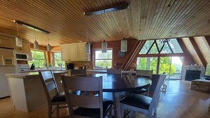 A spacious kitchen with wooden ceiling and large windows, a dining area with a round table and chairs, and a stone fireplace in the living room. - 4 Bedrooms, Heated Private pool, hot tub, Game room, and Water Front View! (Monticello)