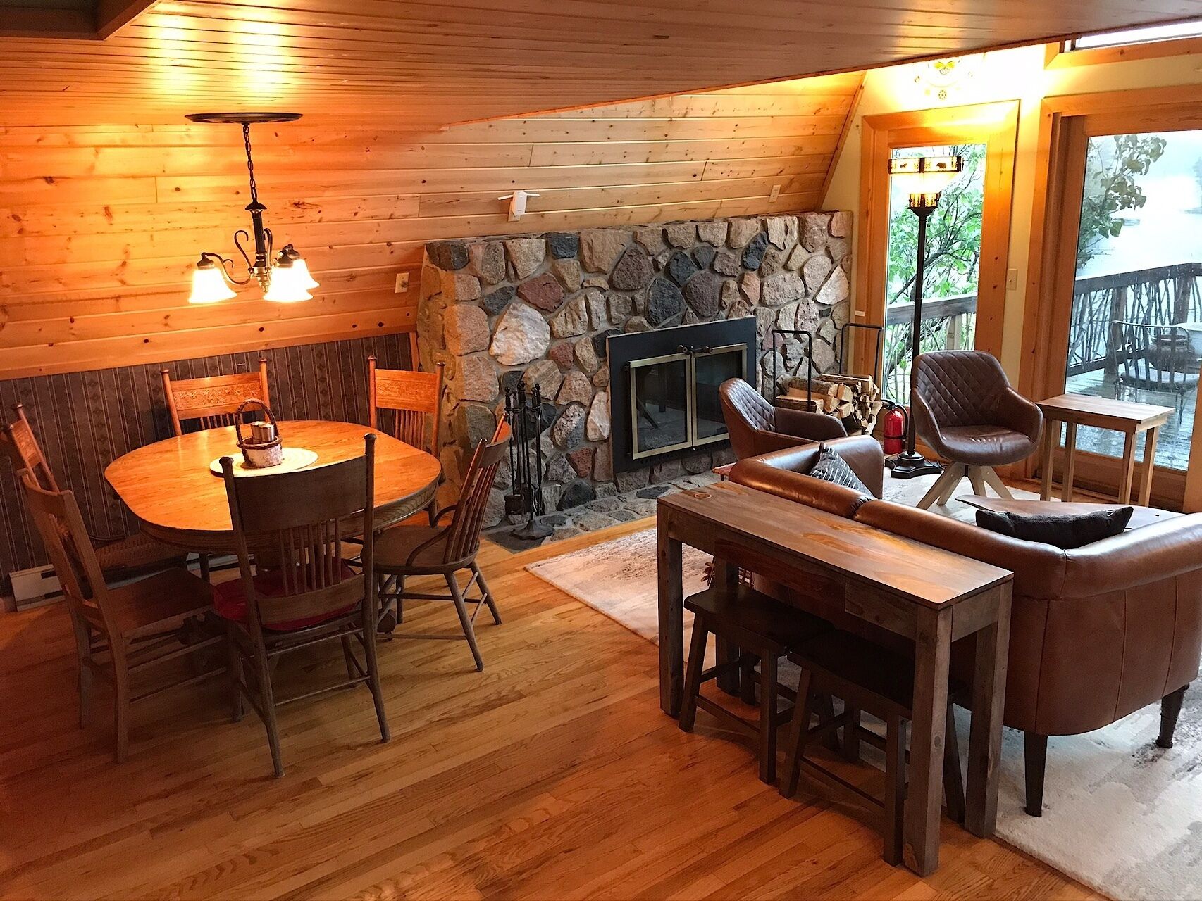 Un intérieur de chalet chaleureux avec une cheminée en pierre, une table à manger en bois et des sièges confortables.