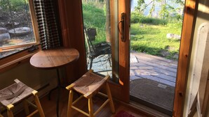 Een kamer met een houten tafel en twee stoelen, een raam met uitzicht op een meer en groen, en een deur met een metalen hendel.