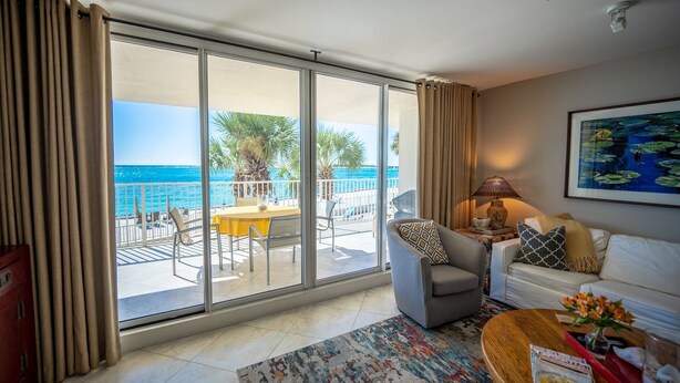 A spacious living area with a balcony overlooking the sea, a sofa, a coffee table, and a dining table with chairs. - Incred Panoramic Gulf View - Sunsets, Water, Private Beach,E Pass Area, Boatslip (Destin)