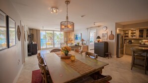 A spacious living area with a dining table, chairs, and a kitchen area with cabinets and appliances. - Incred Panoramic Gulf View - Sunsets, Water, Private Beach,E Pass Area, Boatslip (Destin)