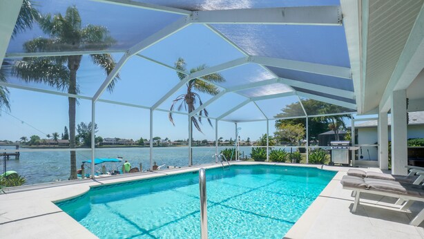 A pool with a glass enclosure, palm trees, and a view of the water. - Lake Home With Heated Pool In Perfect Location (Cape Coral)