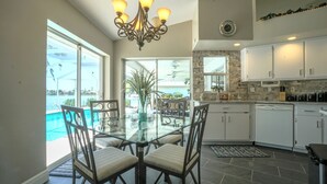 Une cuisine moderne avec des meubles blancs, une table à manger en verre et une vue sur une piscine.