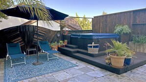 Une terrasse avec un parasol bleu, deux chaises longues, une petite table et des plantes en pot.