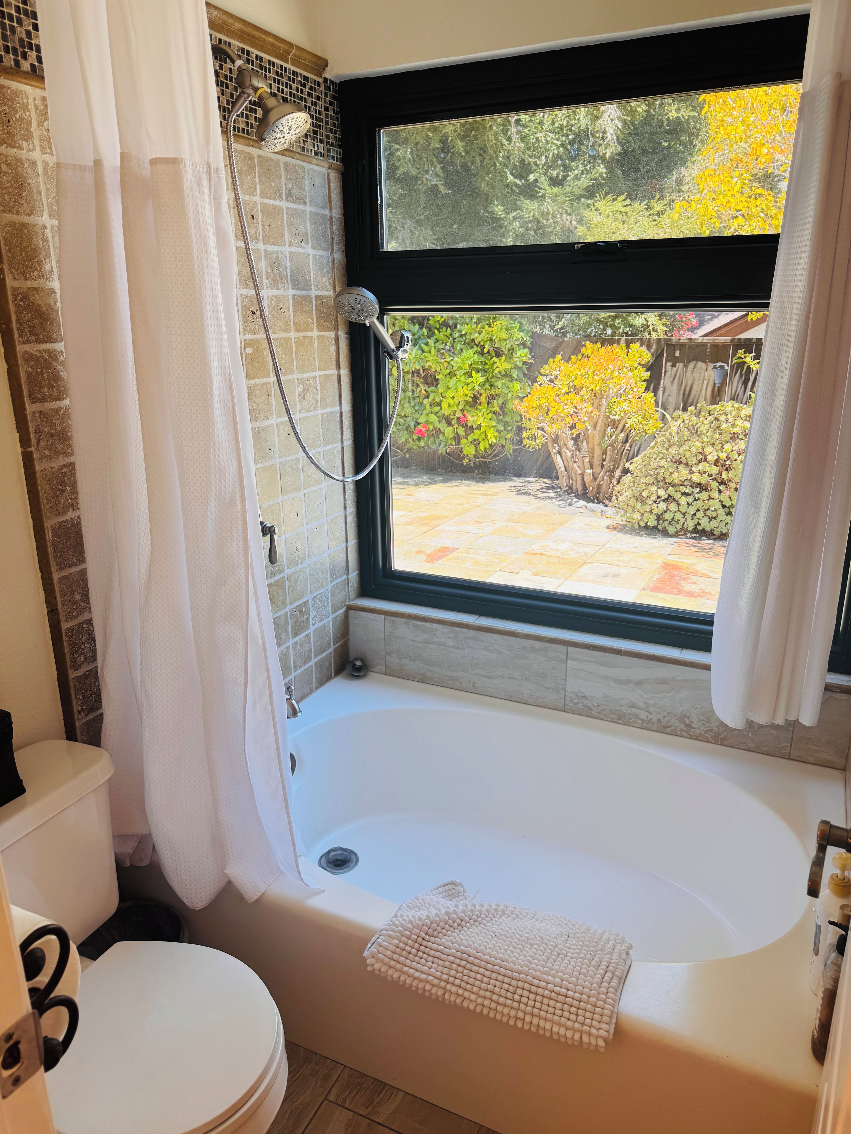 Un baño con bañera, inodoro y ventana con vistas a un jardín.