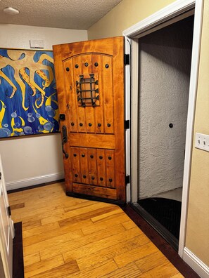 A wooden door with a decorative panel and a small window, leading to a room with a textured wall and a light switch. - SLO Getaway • Hot Tub • 5BR Excellent for Family, Friends and Wedding Groups (San Luis Obispo)