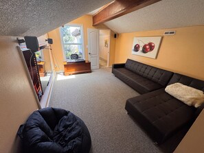 A cozy living room with a dark sofa, a bean bag chair, a small table with a sign, and a window with a view. - SLO Getaway • Hot Tub • 5BR Excellent for Family, Friends and Wedding Groups (San Luis Obispo)