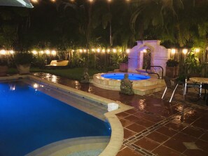 A nighttime pool area with a fountain, surrounded by potted plants and illuminated by string lights. - Downtown,Italian Villa For Two,Resort Style.5 minutes to Siesta-Lido. (Sarasota)