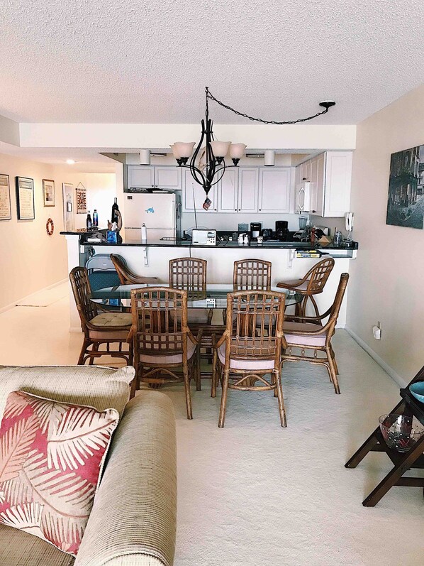 A modern kitchen with white cabinets, a central island, and a dining area with wicker chairs.