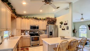 Una cocina moderna con armarios blancos, electrodomésticos de acero inoxidable, una isla central con sillas y ventiladores de techo.