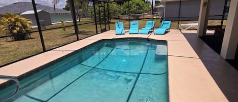 A covered swimming pool with clear blue water, surrounded by a shaded area with lounge chairs.