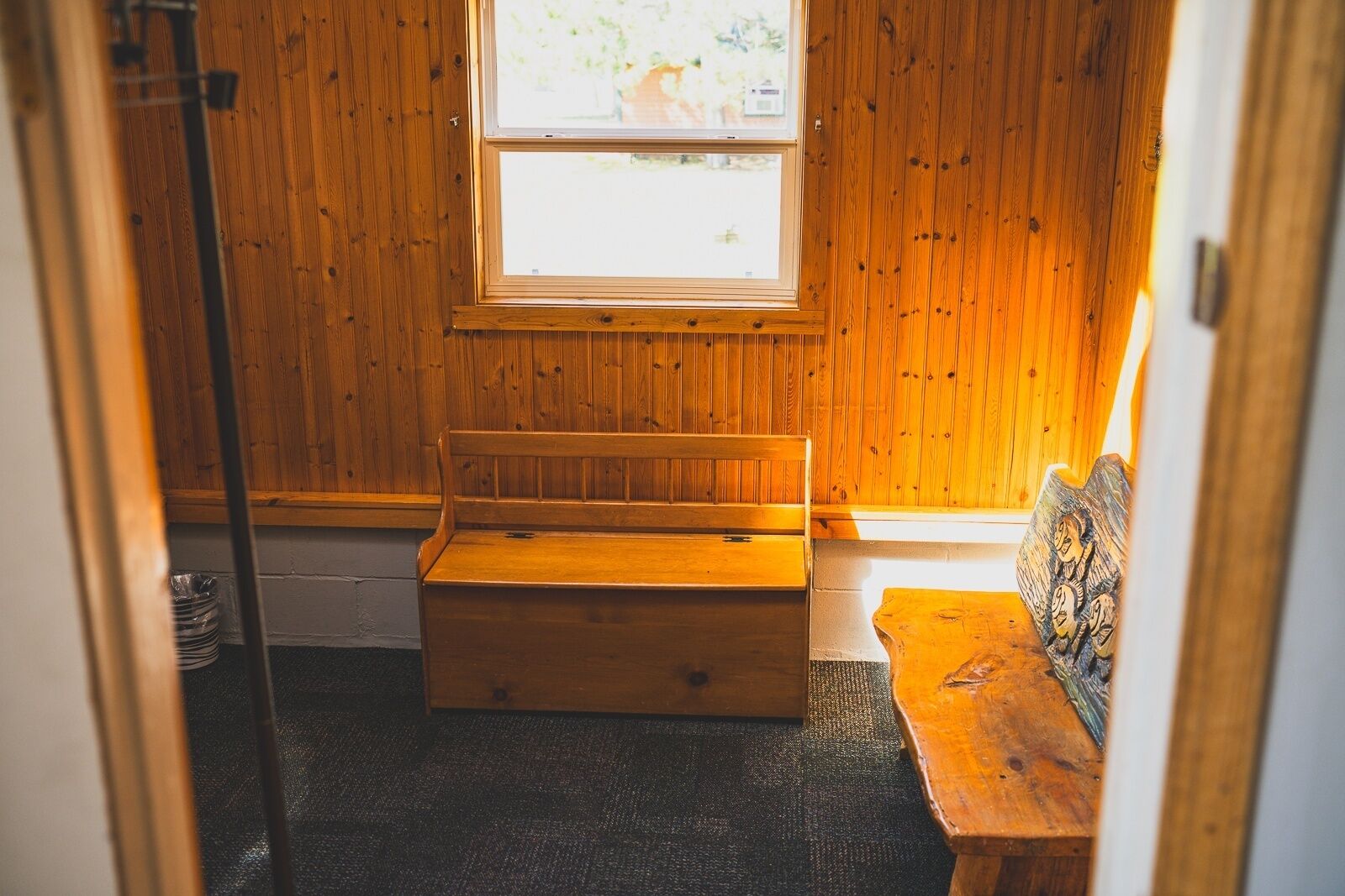 A cozy room with wooden walls, a bench, a small table, and a window with a view.