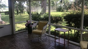 A conservatory with a wicker chair, a small table, and a vase of flowers.