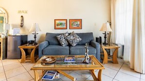 Een woonkamer met een bank, twee ingelijste foto’s, een bijzettafeltje en een lamp.