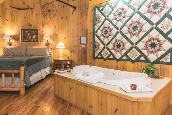 Une pièce en bois avec un lit, une grande couverture, une baignoire et une petite table sur laquelle se trouvent des verres et une bougie.