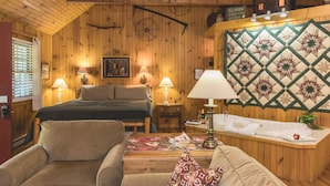 Interior acogedor de una cabaña con techo de madera, una cama, un sofá, una mesa con colcha y un cartel que indica alquiler de cabañas.