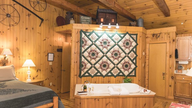 Interior de una cabaña de madera con una cama, un banco con toallas, un tapiz acolchado y un cartel anunciando cabañas en alquiler.