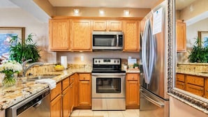 Una cocina con armarios de madera, electrodomésticos de acero inoxidable, encimeras de granito y piso de baldosas.