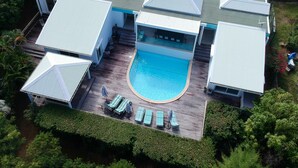 Uma casa moderna com piscina, várias áreas cobertas e um deck com espreguiçadeiras.