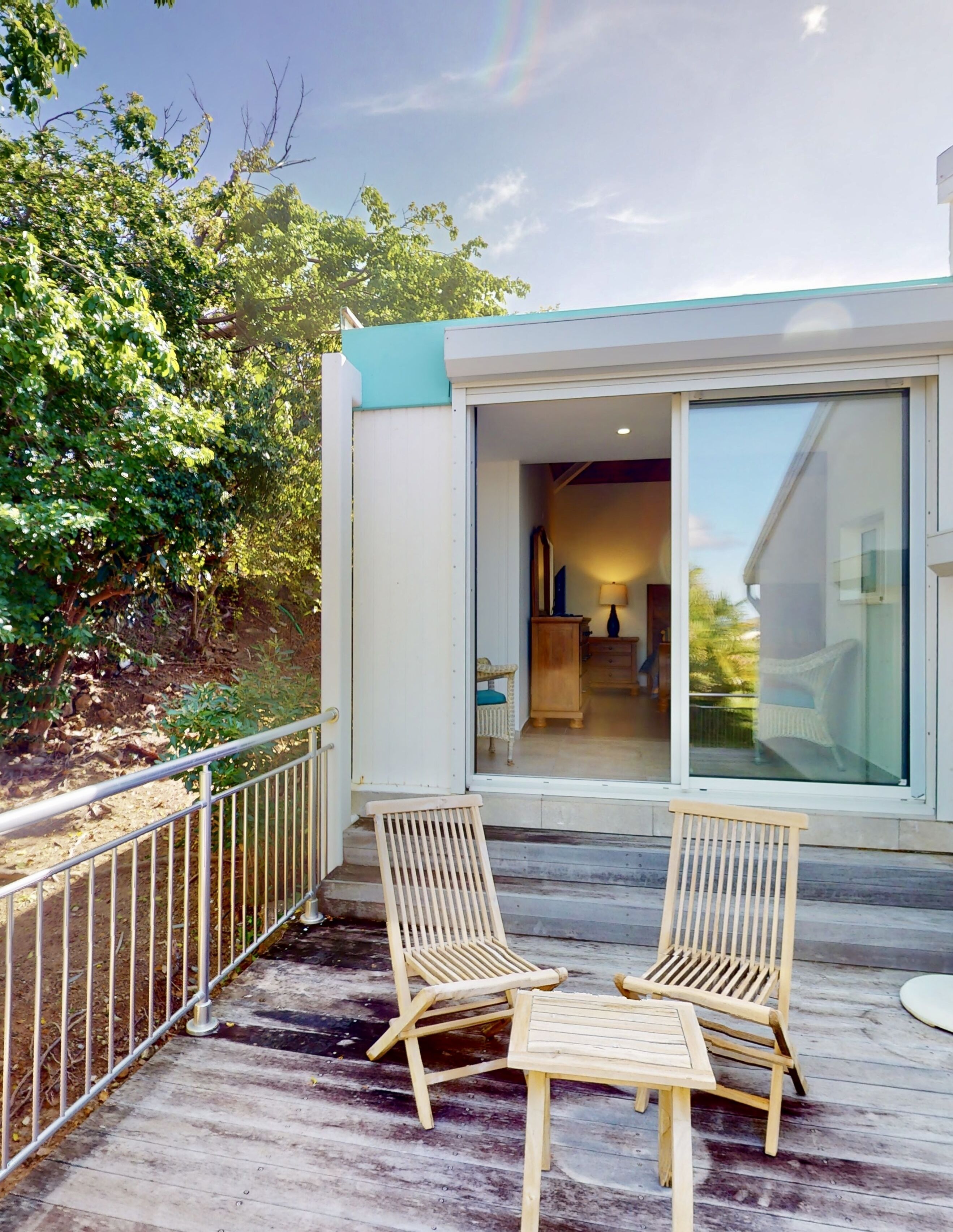 Une maison moderne dotée d’une terrasse, de deux chaises en bois et d’une porte vitrée donnant sur un intérieur comprenant une lampe et une chaise.