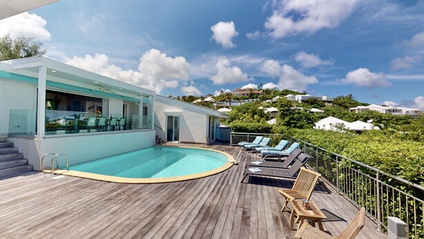 Uma área de piscina moderna com deck de madeira, espreguiçadeiras e um espaço com paredes de vidro que oferece vista para a paisagem ao redor.