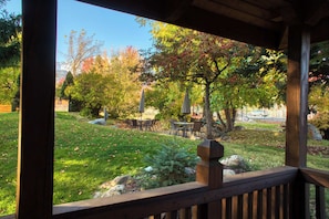 Une terrasse en bois offrant une vue sur un espace vert aménagé en parc, avec une table, des chaises et une sculpture en pierre.