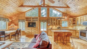 Una cabaña espaciosa de madera con un amplio comedor, una sala de estar acogedora con un sofá de cuero y una cocina con armarios de madera y una isla central.