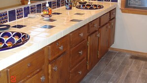 Una cocina con una isla grande, armarios de madera, salpicadero de azulejos y una ventana con vistas a árboles.