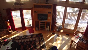 Un salón amplio con un televisor grande, muebles de madera y vistas a una terraza exterior nevada.