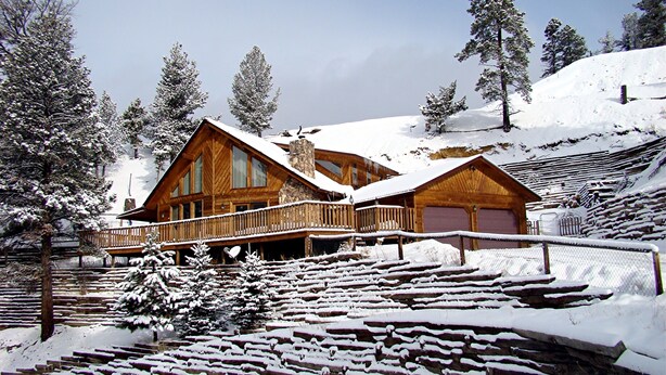 Una cabaña de madera con balcón, rodeada de árboles nevados y un cielo despejado.