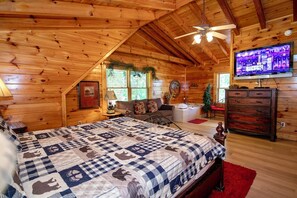Une chambre située dans un chalet en rondins, avec un grand lit, un ventilateur de plafond, une télévision et une cheminée.