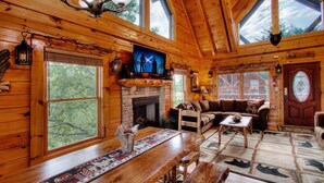 A cozy cabin interior with a fireplace, wooden furniture, large windows, and a ceiling fan. - A+ Views & Location! Minutes 2 Dollywood. Hot Tub Games Pet Friendly Resort Pool (Pigeon Forge)