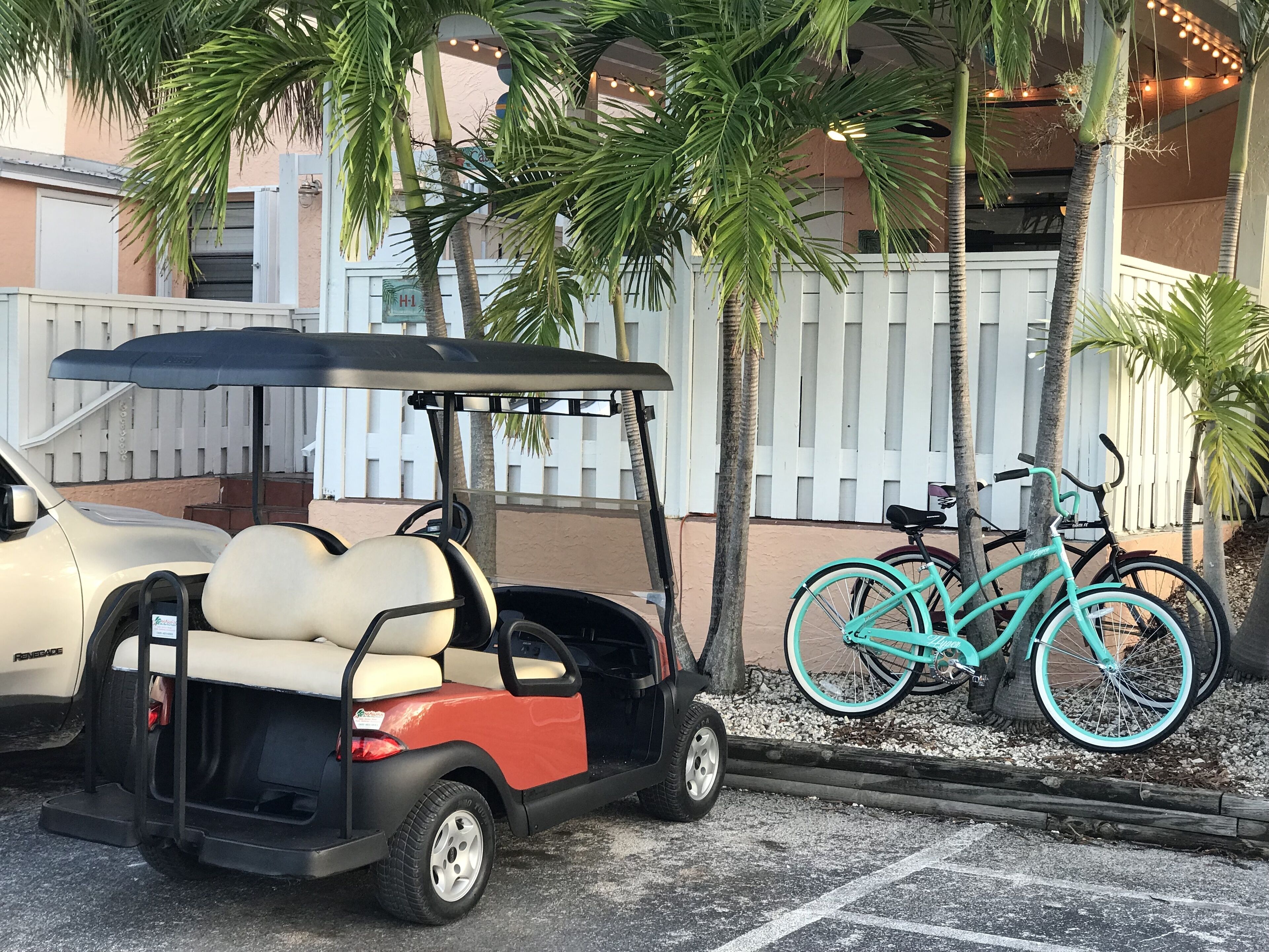 Carrinho de golfe estacionado ao lado de uma cerca branca, com bicicletas.