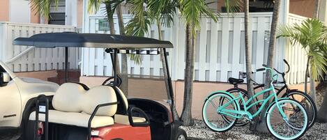 Carrinho de golfe estacionado ao lado de uma cerca branca, com bicicletas.