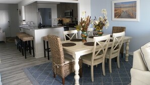 Een eetruimte met een witte tafel, rieten stoelen en een keuken op de achtergrond.