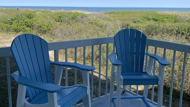 Twee Adirondack-stoelen op een balkon met uitzicht op zee en strand.