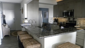 Een moderne keuken met een centraal eiland, roestvrijstalen apparatuur en rieten barstoelen.