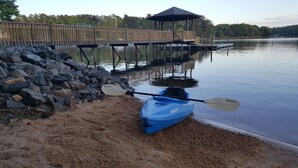 A kayak with paddles on a sandy shore by a calm lake, a wooden dock, and a gazebo in the background. - Lake Front Getaway, Family Friendly. (Mooresville)